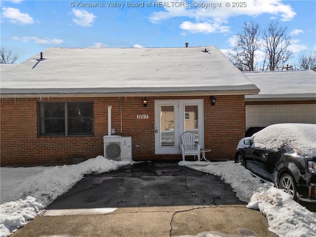 snow covered property entrance with a garage and ac unit