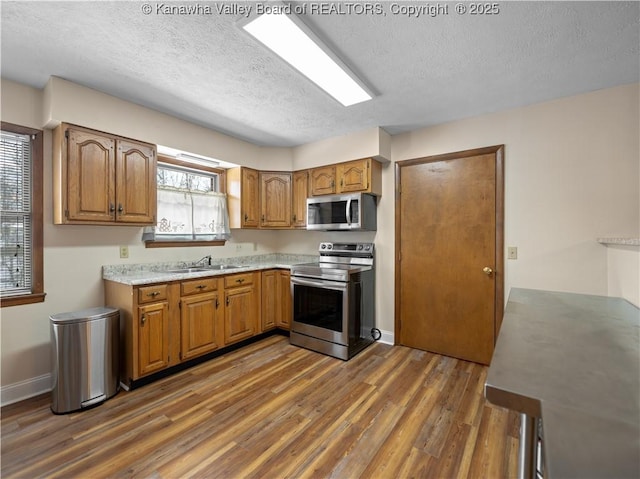 kitchen with appliances with stainless steel finishes, sink, a textured ceiling, and dark hardwood / wood-style floors