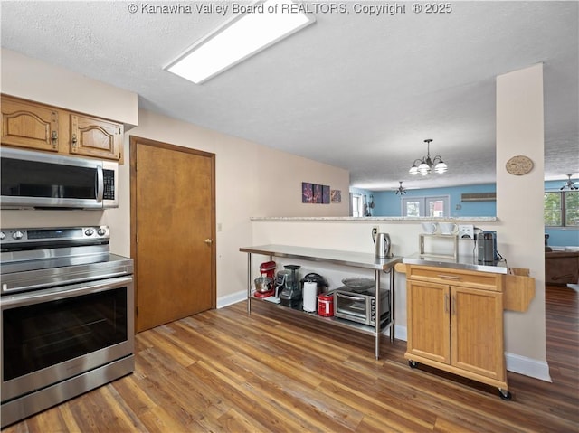 kitchen with kitchen peninsula, appliances with stainless steel finishes, dark hardwood / wood-style floors, decorative light fixtures, and a notable chandelier