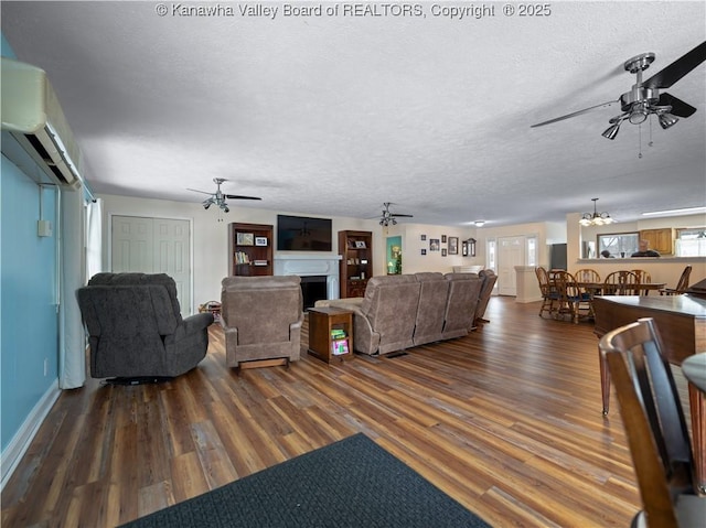 living room with a wall unit AC, dark wood-type flooring, a textured ceiling, and ceiling fan with notable chandelier