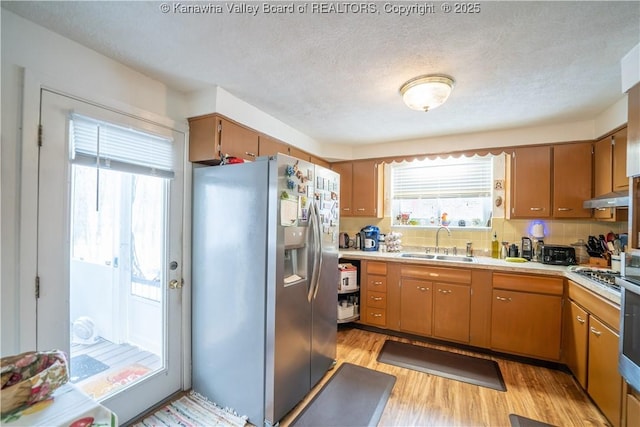 kitchen featuring backsplash, sink, light hardwood / wood-style flooring, appliances with stainless steel finishes, and a textured ceiling