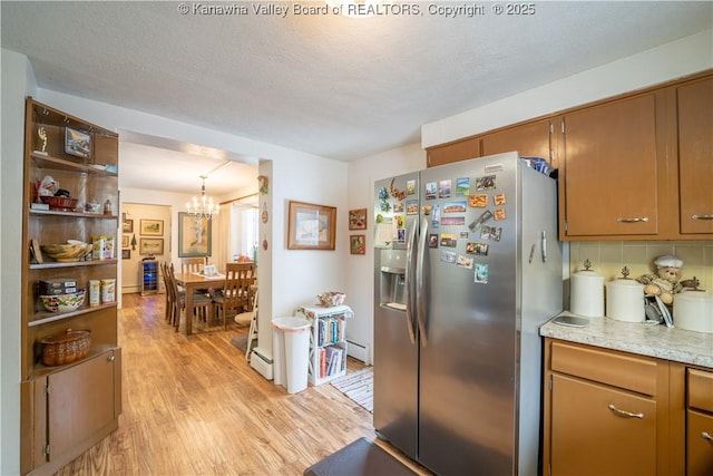 kitchen featuring baseboard heating, stainless steel refrigerator with ice dispenser, decorative backsplash, a chandelier, and light hardwood / wood-style flooring