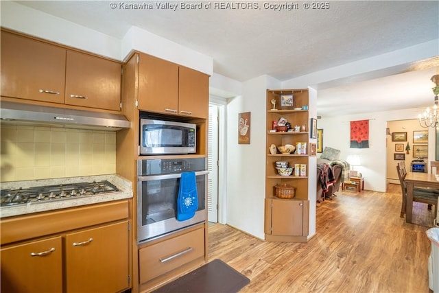 kitchen featuring backsplash, appliances with stainless steel finishes, an inviting chandelier, and light hardwood / wood-style floors