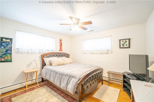 bedroom featuring ceiling fan, a baseboard heating unit, and light hardwood / wood-style flooring