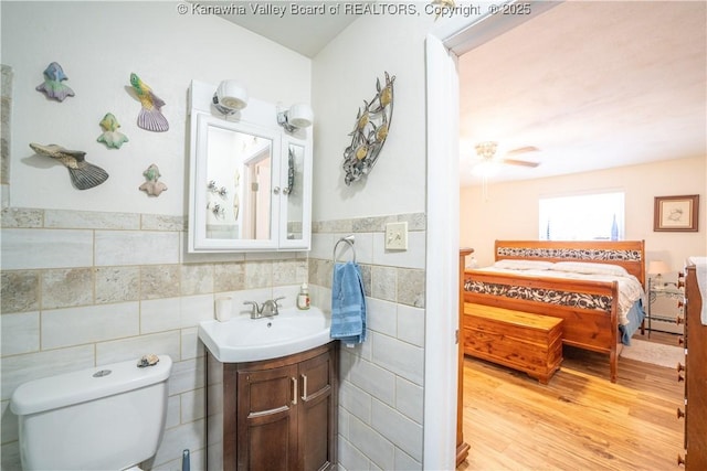 bathroom with baseboard heating, hardwood / wood-style floors, vanity, tile walls, and toilet