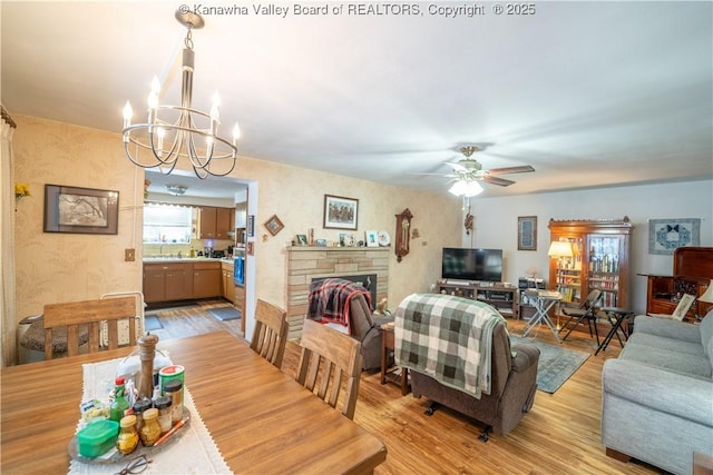 dining area featuring ceiling fan with notable chandelier, light hardwood / wood-style flooring, and a stone fireplace