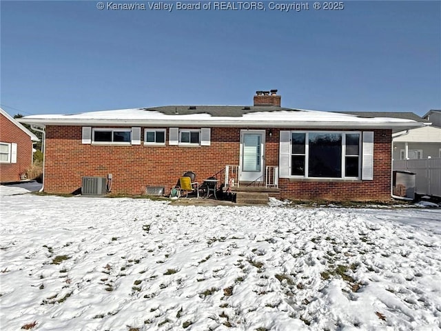 snow covered rear of property featuring central AC unit