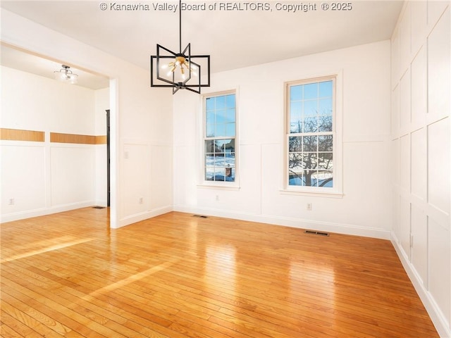 unfurnished dining area featuring an inviting chandelier and light hardwood / wood-style flooring