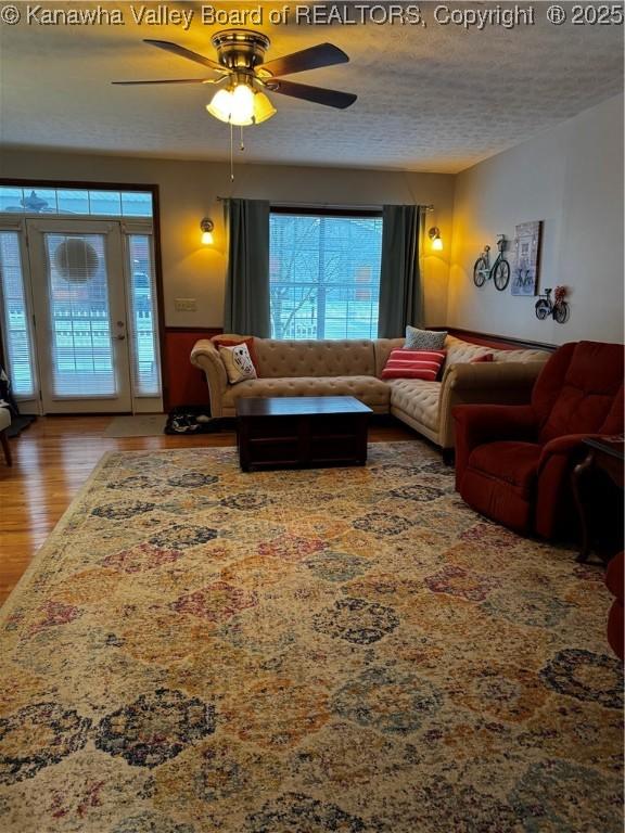 living room with ceiling fan, a textured ceiling, hardwood / wood-style floors, and a healthy amount of sunlight