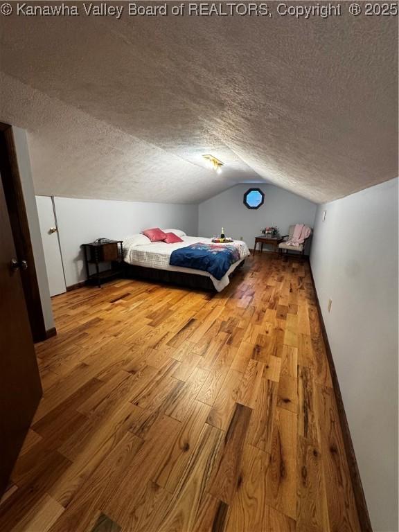 unfurnished bedroom featuring vaulted ceiling, a textured ceiling, and hardwood / wood-style floors