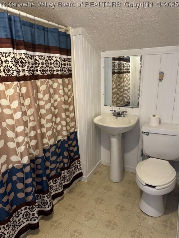 bathroom with toilet, a shower with curtain, sink, and a textured ceiling