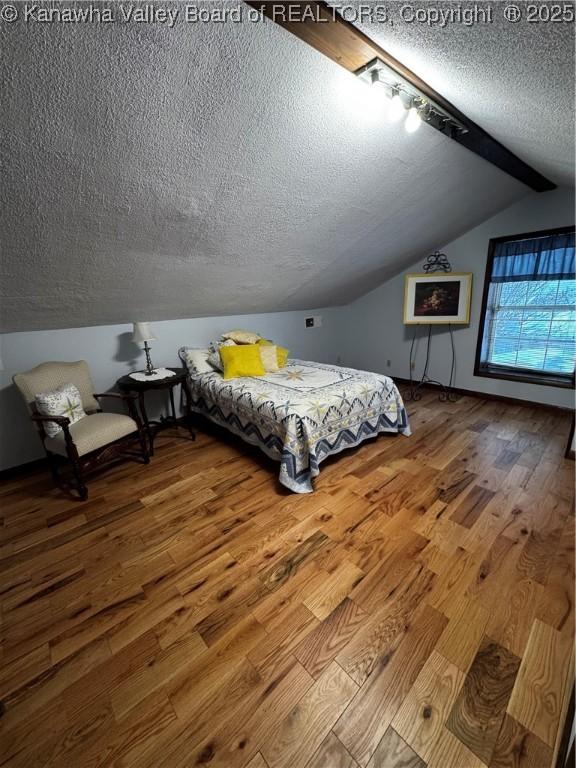 bedroom featuring a textured ceiling, vaulted ceiling with beams, and hardwood / wood-style floors