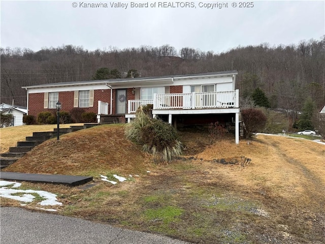 view of front of property with a deck, brick siding, and a wooded view