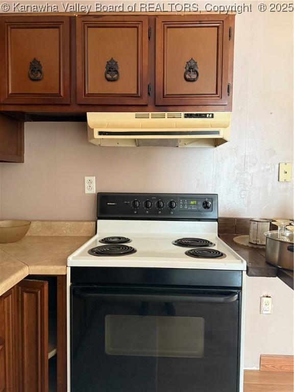 kitchen with light countertops, range with electric stovetop, brown cabinetry, and under cabinet range hood