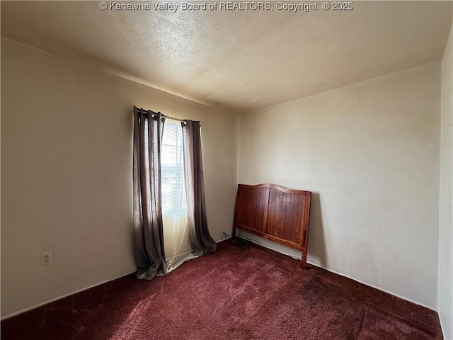 spare room with a textured ceiling and dark colored carpet