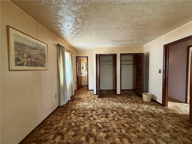 unfurnished bedroom featuring carpet flooring, a textured ceiling, baseboards, and two closets