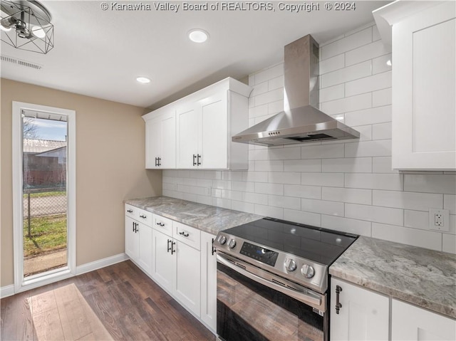 kitchen with stainless steel electric range oven, backsplash, wall chimney range hood, and white cabinetry