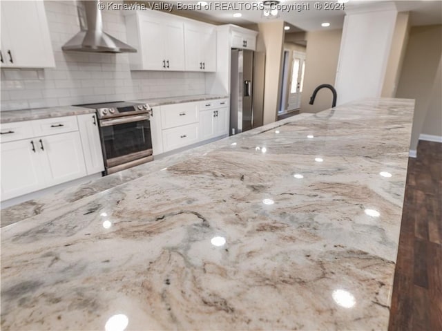 kitchen featuring white cabinets, wall chimney exhaust hood, light stone counters, and stainless steel appliances