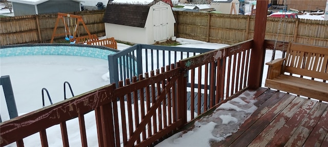 snow covered deck with a storage unit and a fenced in pool