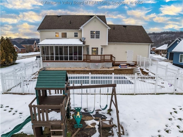 snow covered back of property with a sunroom and a playground