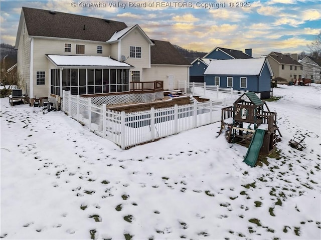 snow covered rear of property with a sunroom and a playground