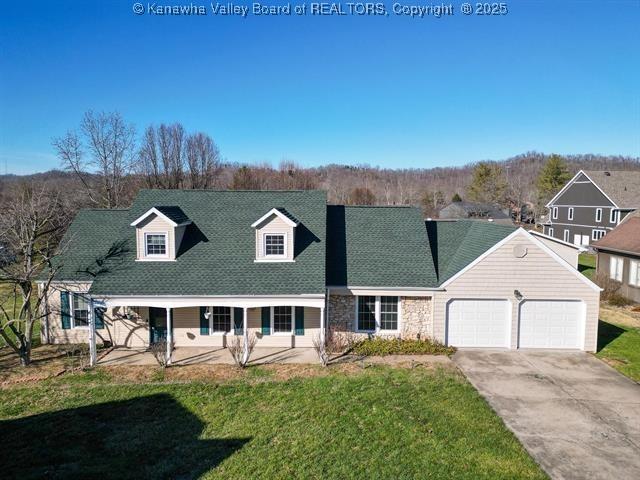 cape cod house featuring driveway, stone siding, roof with shingles, an attached garage, and a front yard