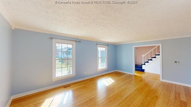 empty room featuring wood-type flooring, ornamental molding, and a textured ceiling