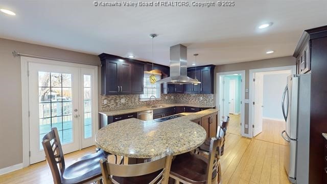 kitchen with appliances with stainless steel finishes, backsplash, light wood-style flooring, and island range hood