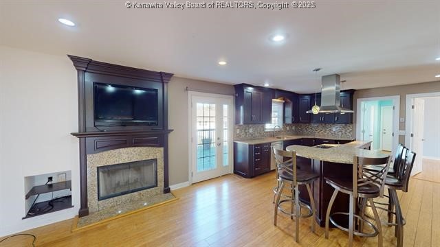 kitchen with decorative backsplash, a sink, wall chimney range hood, and light wood finished floors