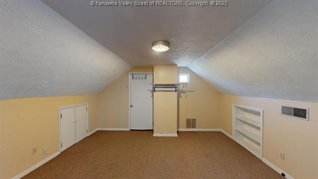 bonus room with built in shelves, lofted ceiling, visible vents, and a textured ceiling