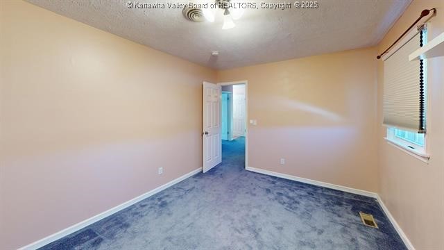 empty room with carpet floors, visible vents, a textured ceiling, and baseboards