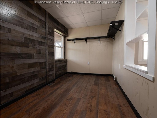 spare room with a paneled ceiling, dark hardwood / wood-style flooring, and wooden walls