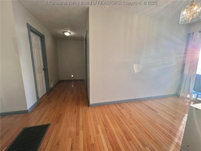 unfurnished room featuring a textured ceiling, a chandelier, and light wood-type flooring