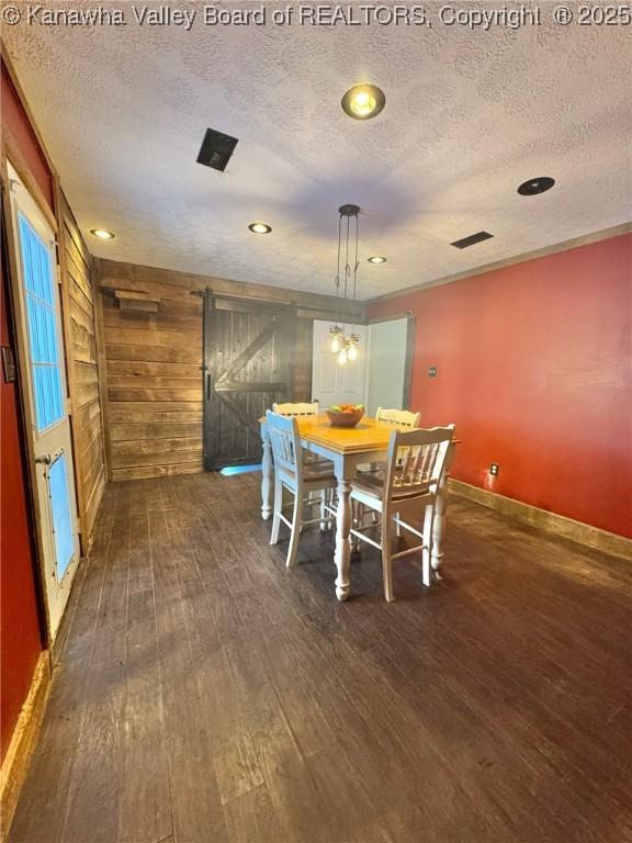 dining space featuring a textured ceiling, dark hardwood / wood-style flooring, a barn door, and wood walls