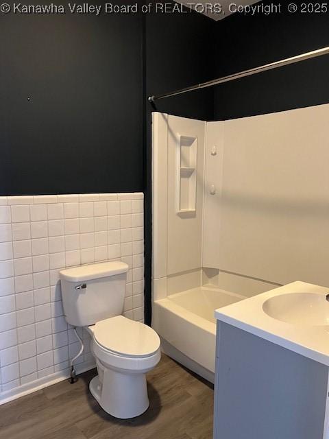 full bathroom featuring shower / bathing tub combination, tile walls, toilet, and hardwood / wood-style floors