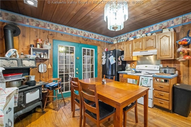 kitchen with black refrigerator, white range with electric stovetop, a wood stove, light wood-type flooring, and french doors