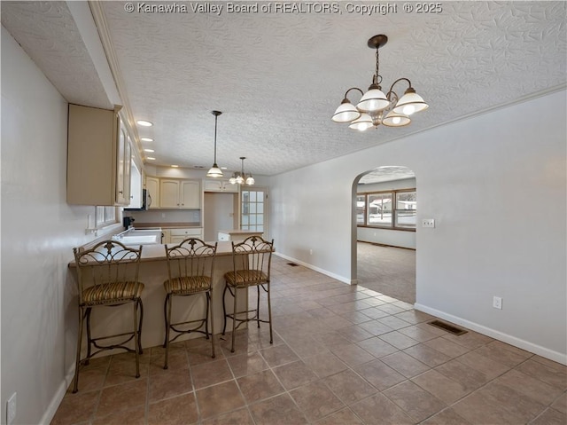 kitchen with a kitchen breakfast bar, a textured ceiling, an inviting chandelier, and kitchen peninsula