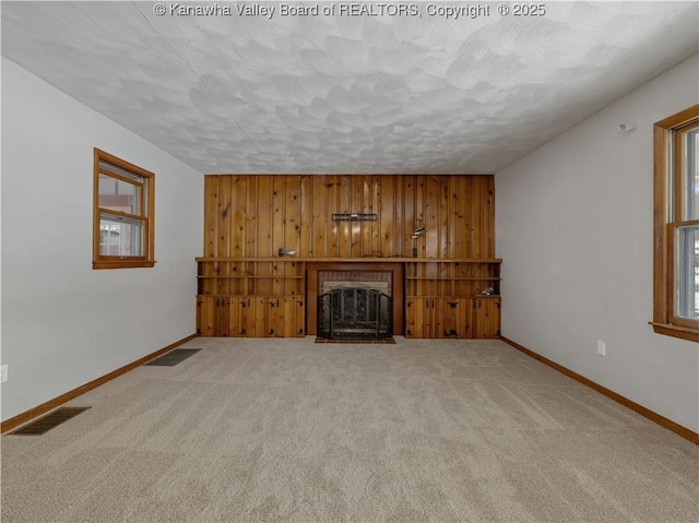 unfurnished living room with carpet flooring, a textured ceiling, and wood walls