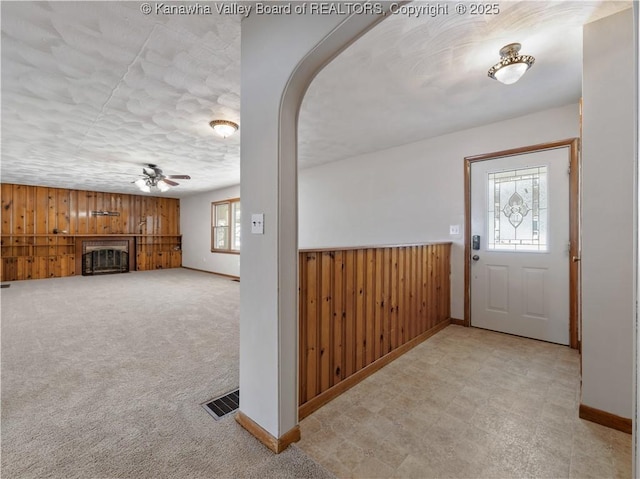 carpeted foyer entrance featuring a wealth of natural light, wooden walls, and ceiling fan