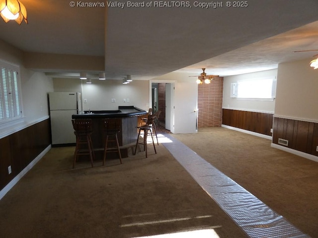 dining room with dark colored carpet, ceiling fan, bar area, and wood walls