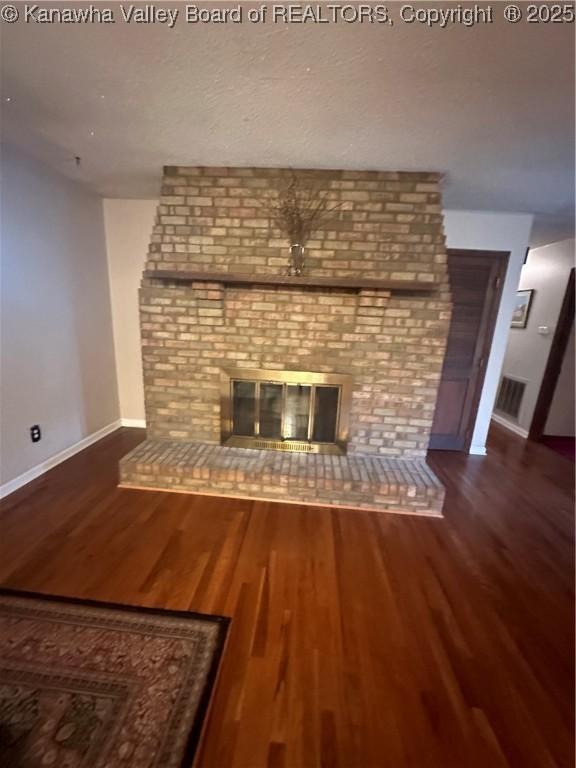 unfurnished living room with wood-type flooring and a brick fireplace