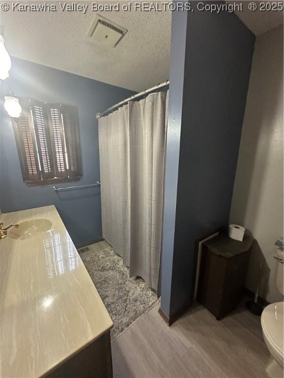 bathroom with curtained shower, hardwood / wood-style flooring, vanity, toilet, and a textured ceiling