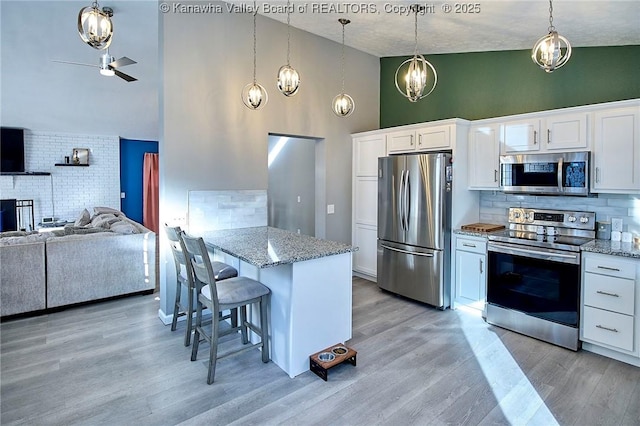 kitchen with white cabinetry, hanging light fixtures, light hardwood / wood-style flooring, a kitchen breakfast bar, and stainless steel appliances