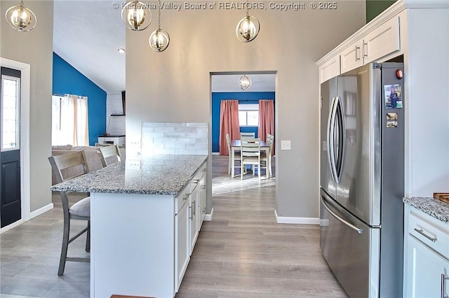 kitchen with white cabinetry, vaulted ceiling, a kitchen bar, and stainless steel refrigerator