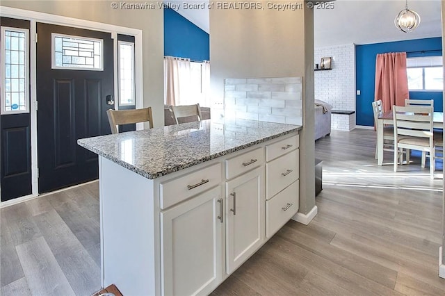 kitchen with white cabinetry, decorative light fixtures, light stone counters, and light hardwood / wood-style flooring