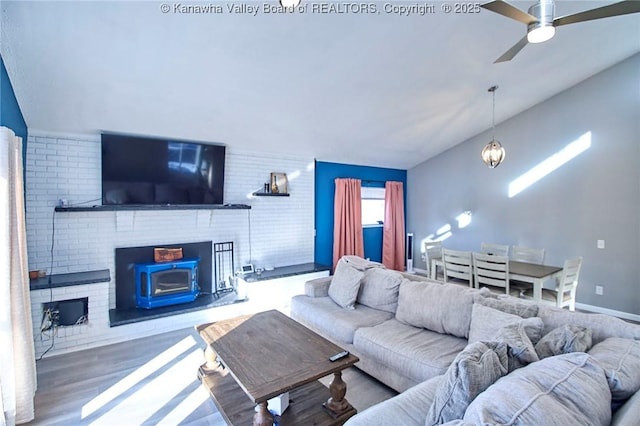 living room with ceiling fan with notable chandelier, brick wall, hardwood / wood-style floors, and lofted ceiling