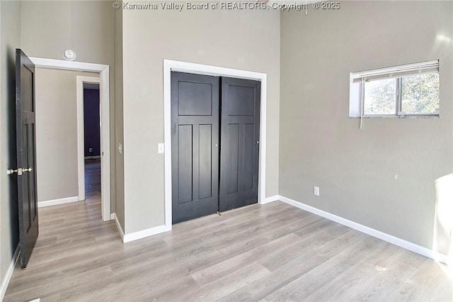 unfurnished bedroom featuring a towering ceiling, light hardwood / wood-style floors, and a closet