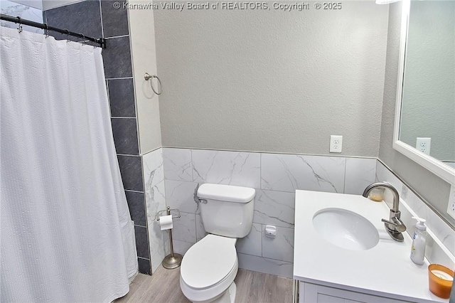 bathroom featuring tile walls, hardwood / wood-style flooring, vanity, toilet, and a shower with curtain