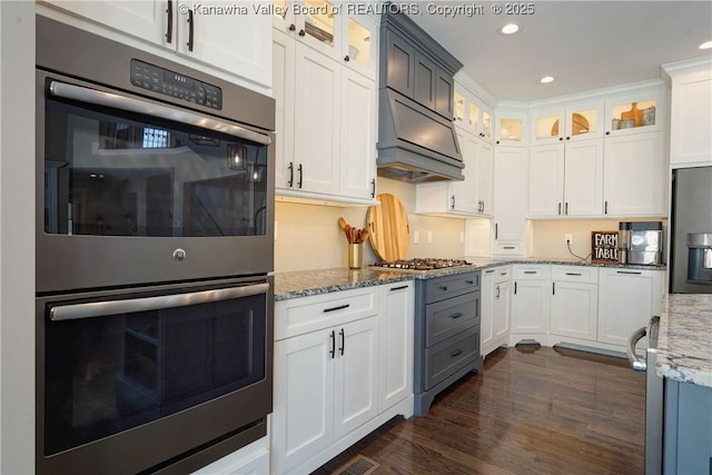 kitchen featuring light stone countertops, custom range hood, white cabinets, and appliances with stainless steel finishes