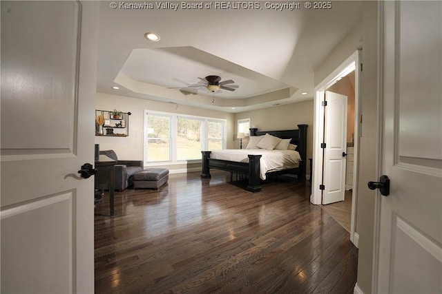 bedroom with dark wood-type flooring, ceiling fan, and a tray ceiling